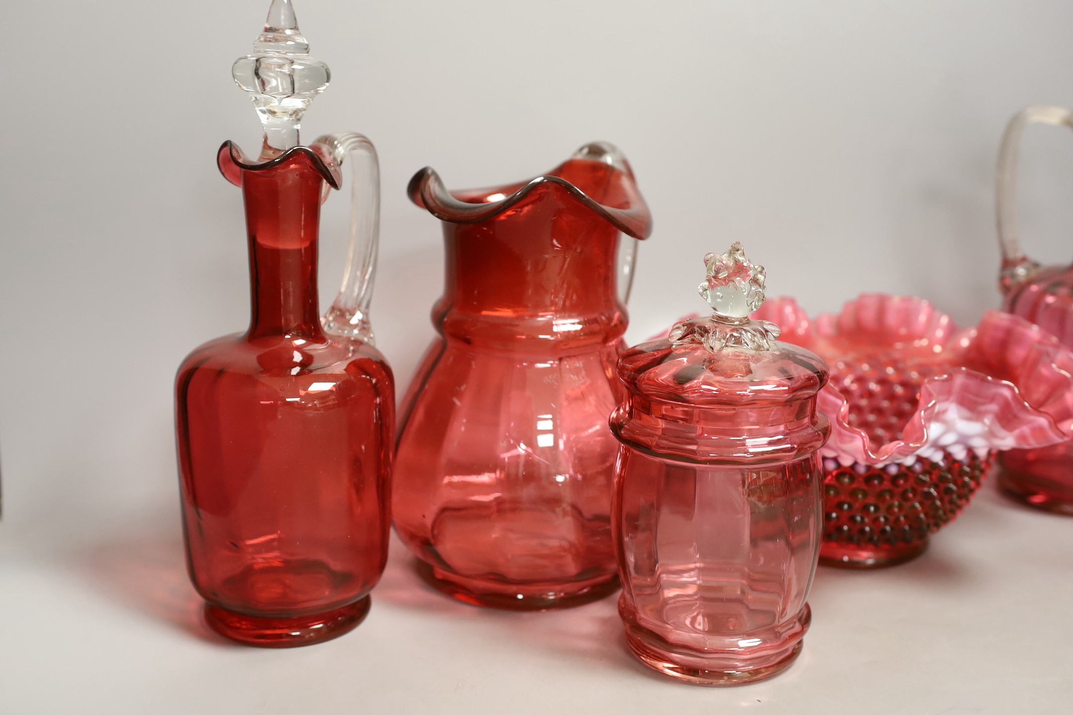 A pair of cranberry glass decanters, a jug, a fluted vase and a biscuit box and cover- decanters and stoppers 28cms high.